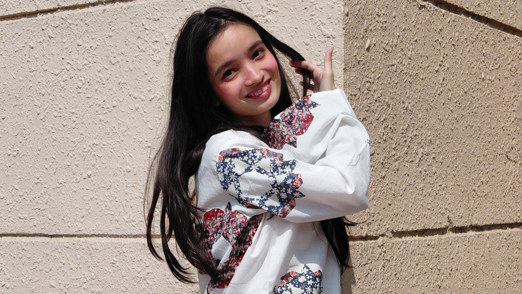 Young girl with floral sleeves posing against a beige wall