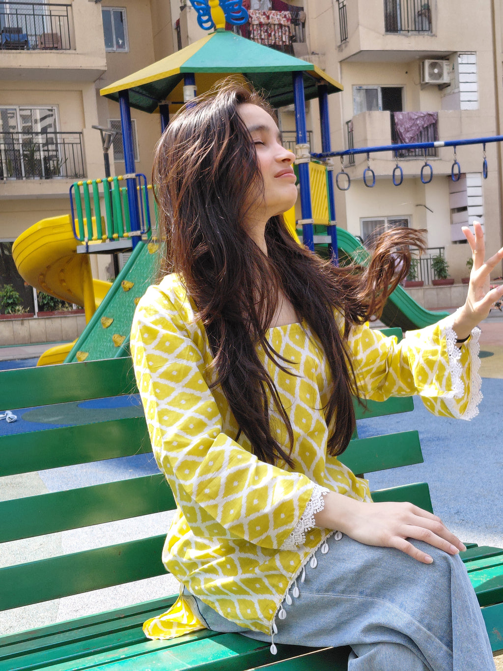 Person in a yellow patterned outfit sitting on a colorful bench inside a building.